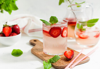 Homemade refreshing strawberry lemonade in glasses and jug with fresh strawberries and mint leaves. Summer drink 
