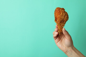Female hand holds fried chicken on mint background