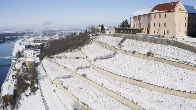 Vineyard terraces below a church by a river with bridge in winter snow.