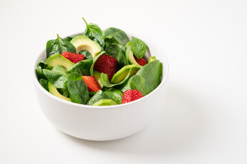 Strawberry salad with avocado and spinach. Summer salad in bowl on white plate, side view