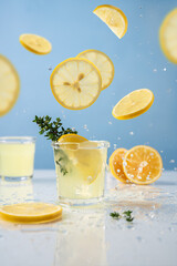 Limoncello in glass on blue background. Falling lemon slices and splashes. Summer background