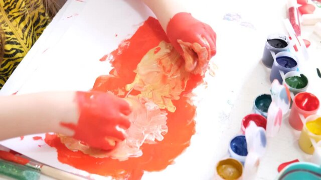 little girl having fun painting her hands . Funny child draws hands dirty with red paint. 