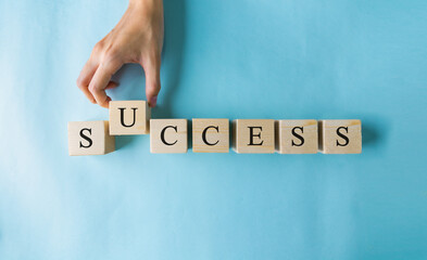 Hand of woman holding over the wooden cubes with the word SUCCESS.