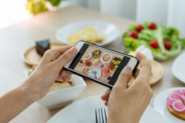 A reviewer's hand using a mobile phone to take pictures of food at a restaurant table.Take photo to...