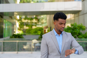 Fototapeta premium Young African businessman outdoors checking time from watch