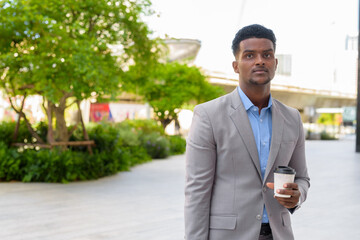 Handsome young African businessman outdoors carrying cup of take away coffee