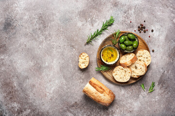 Fresh Italian ciabatta bread in slices on a wooden plate with olive oil, olives and herb, beige rustic background. Top view, flat lay.