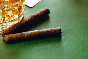 Close up of whiskey glass and cigar on green background