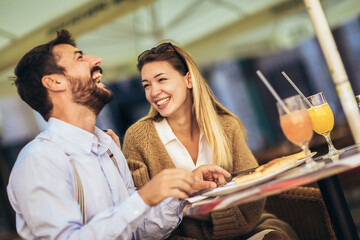 Attractive and happy young couple having good time in cafe restaurant. They are smiling and eating a pizza.