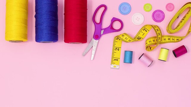 Sewing craft materials appear on pastel pink background. Stop motion flat lay