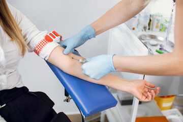 Laboratory and blood analysis concept. Close up cropped shot of professional nurse in gloves, taking a blood sample from arm vein of young female patient - obrazy, fototapety, plakaty