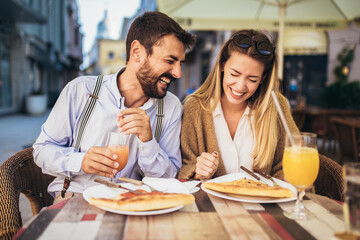 Fototapeta na wymiar Attractive and happy young couple having good time in cafe restaurant. They are smiling and eating a pizza.