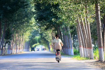 Fototapeta na wymiar A woman rides an electric car on a country road in North China