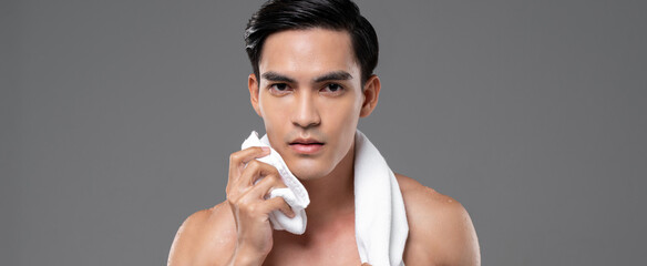 Young handsome shirtless Southeast Asian man wiping his face with towel in isolated studio gray...