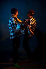 Two guys in a plaid shirt are holding a girl on a dark background in a studio with multicolored light.