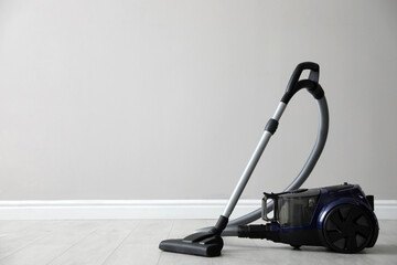 Modern vacuum cleaner near white wall indoors, space for text - obrazy, fototapety, plakaty