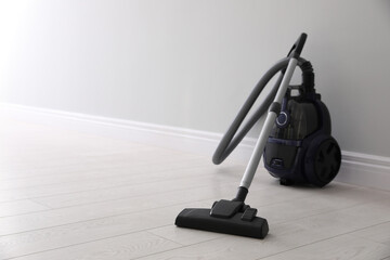 Modern vacuum cleaner near light wall indoors, space for text