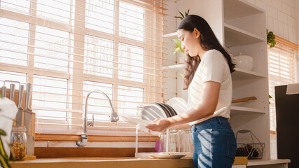 Attractive young Asia lady washing dishes while doing cleaning in the kitchen at house. Stay at...