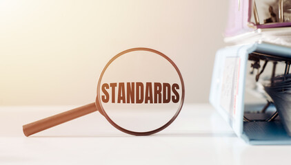 Magnifying glass with the word STANDARDS on office table.