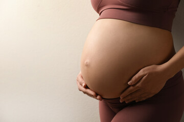 Pregnant young woman touching belly on beige background, closeup. Space for text