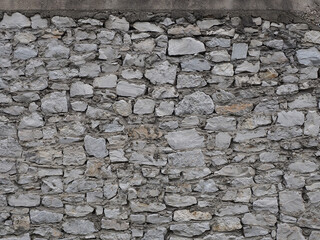 Unplastered wall of rough gray stone of various shapes and sizes. Full screen photo