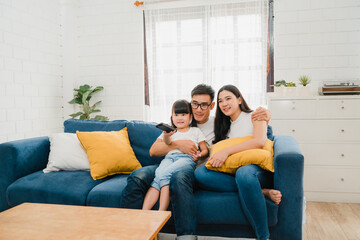 Happy Asian family enjoy their free time relax together at home. Lifestyle Korean dad, mom and daughter watching TV together and having fun lying on sofa in living room in modern house.