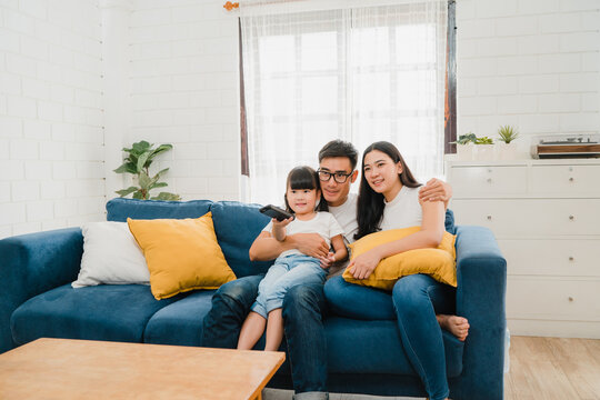 Happy Asian Family Enjoy Their Free Time Relax Together At Home. Lifestyle Korean Dad, Mom And Daughter Watching TV Together And Having Fun Lying On Sofa In Living Room In Modern House.