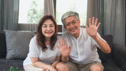 Asian elderly couple using smartphone video conference with grandchild while lying on sofa in...