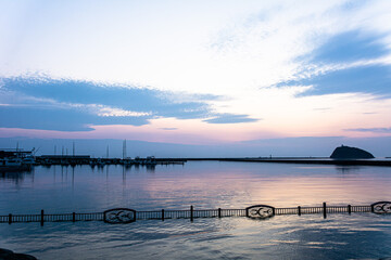 水平線に浮かぶ孤島とヨットの波止場と夕焼けの海と空