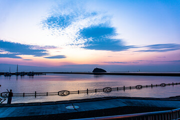 夕焼けの水平線に浮かぶ孤島と、入江と空に浮かぶ青い雲