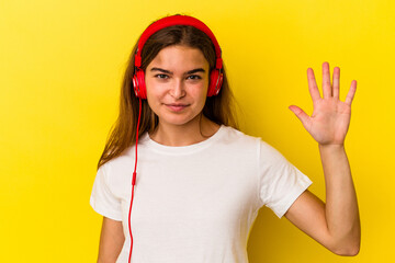 Young caucasian woman listening to music isolated on yellow background smiling cheerful showing number five with fingers.