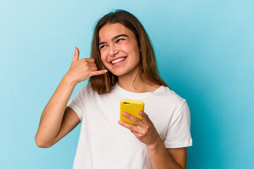 Young caucasian woman holding a mobile phone isolated on blue background showing a mobile phone call gesture with fingers.