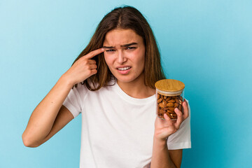 Young caucasian woman holding an almond jar isolated on blue background showing a disappointment...
