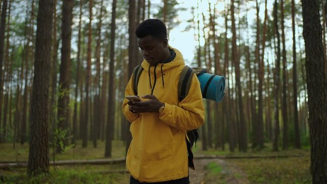 Black man in yellow jacket walks through the woods and talks on the phone with a backpack in slow motion 