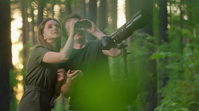 Birdwatching in park. Couple watch birds with binoculars and camera with telephoto lens. Amateur birdwatchers spot birds in the spring park
