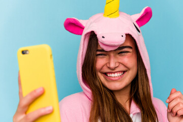 Young caucasian woman wearing a unicorn pajama holding a mobile phone isolated on blue background