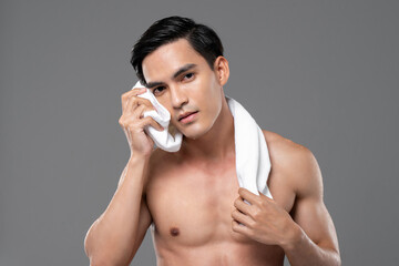 Beauty and skin care portrait of shirtless handsome young Asian man wiping his face with towel...