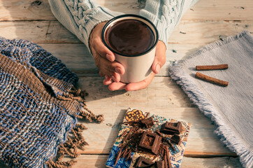 Cup of hot chocolate in woman's hands, cinnamon and pieces of chocolat on wooden rustic table