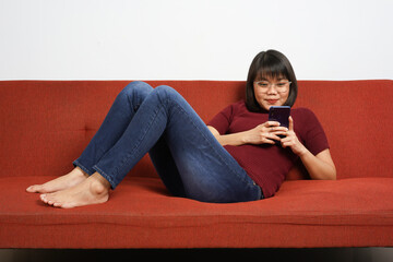 Using smartphone of Young beautiful Asian women dress red shirt and jeans sitting on red couch