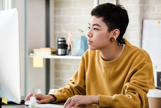 Young Asian tomboy woman in casual attire working from home on laptop computer in living room