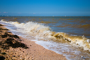 waves crashing on the Isle of Grain beach, Kent, during high tide on a sunny summer afternoon