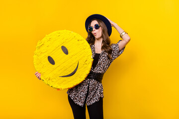 Photo of amazed shocked young woman hold big emoji smile wear hat sunglass isolated on yellow color backgroundq