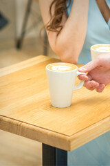 Hand of waiter puts a cup of coffee latte on the wooden table in a cafe