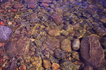 multicolored texture surface of the water stream, clear water, colored stones at the bottom of the river