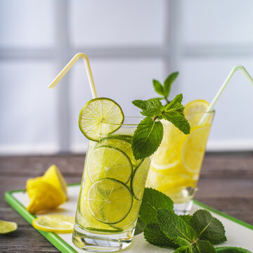 Freshly made lemonade of thinly sliced lime and soda water in curved glass glasses and mint leaves