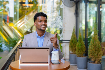African businessman at coffee shop using laptop computer while smiling and pointing finger