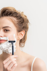 Naklejka premium Beautiful young caucasian smiling woman shaving her face with razor on white background