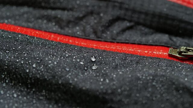 Water droplets on the waterproof fabric. Close-up of a waterproof jacket. Black clothes with red zipper