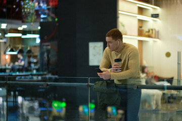 young man using smartphone and listens to music in bluetooth headphones. lonely man in autumn...