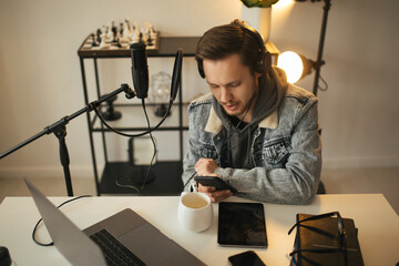 Young man blogger recording online podcast using his laptop, headphones and professional microphone in a studio.